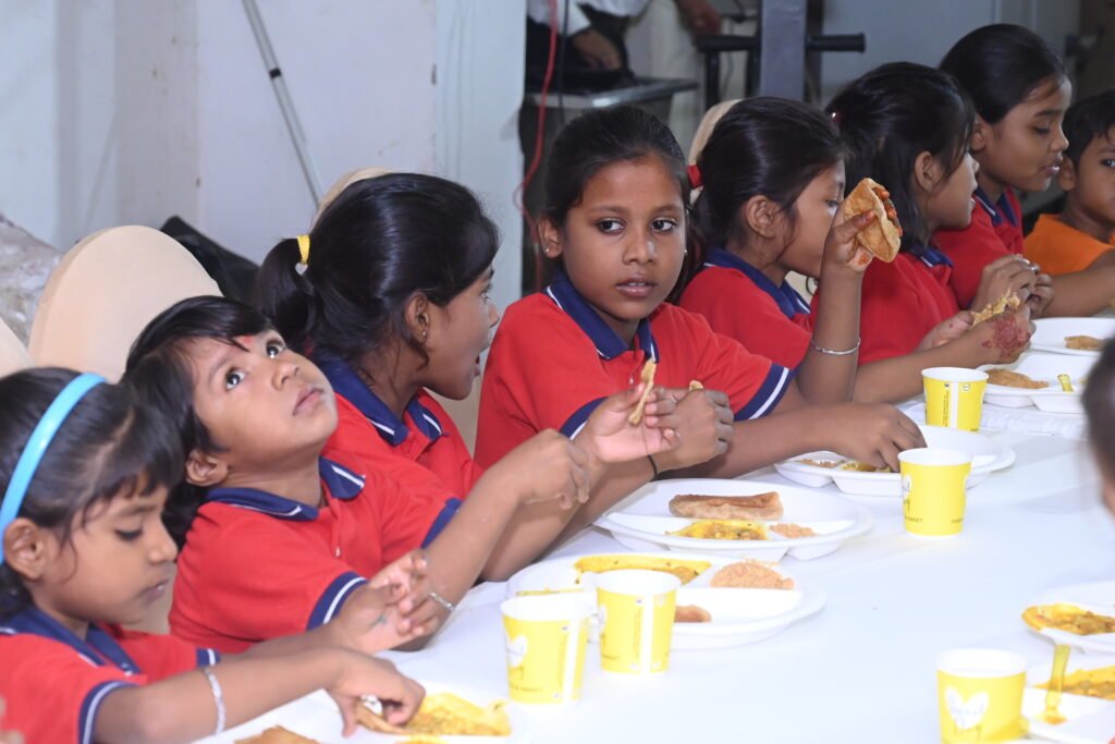 Children of Divine Sanskarshala in red uniforms sitting together and enjoying a meal during a community gathering.