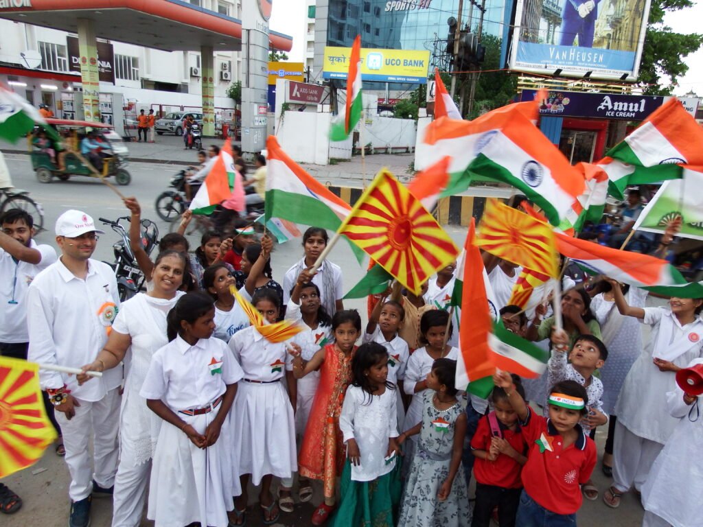 A group of children and volunteers from Divine Sanskarshala waving Indian national flags and spiritual flags during an Independence Day celebration.