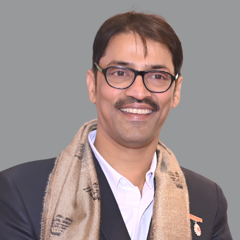 Professional portrait of Anil Agrawal, Core Member of Divine Sanskarshala, smiling warmly while wearing glasses, a formal blazer, and a traditional stole against a plain grey background.