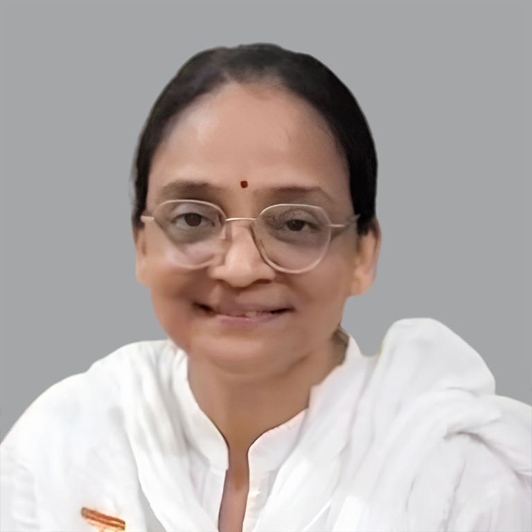 Portrait of Charu Jain, Executive Member of Divine Sanskarshala, smiling gently while dressed in white attire and glasses against a plain grey background.