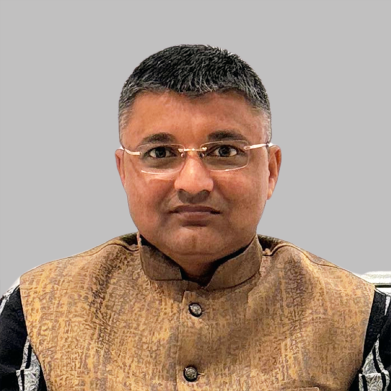 Portrait of Manish Gujarati, Core Member of Divine Sanskarshala, wearing a traditional golden Nehru jacket with glasses against a plain grey background.