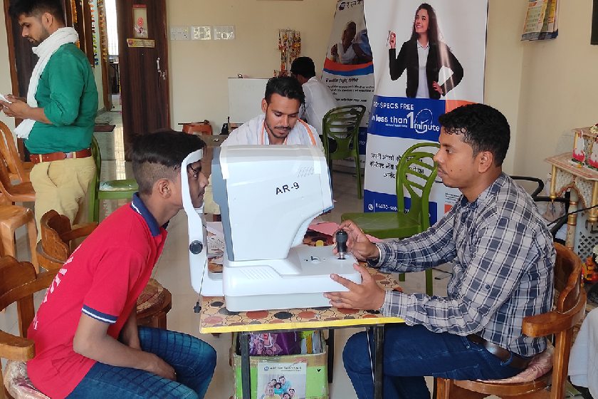 An eye specialist conducts an eye examination for a young boy using diagnostic equipment during a Divine Sanskarshala community health and vision care camp.