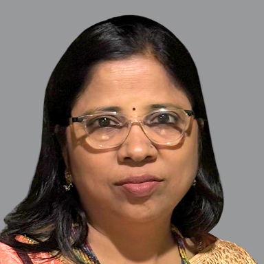 Portrait of Meenakshi Nagar, Executive Member of Divine Sanskarshala, wearing glasses and a traditional outfit against a gray background.