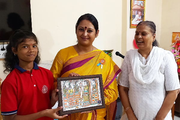 Pooja Dikshit, Regional Minister of BJP Mahila Morcha in Varanasi, receiving a handmade artwork from a student at Divine Sanskarshala while another woman stands beside them during the event.