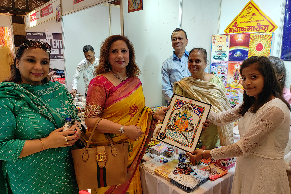Pooja Madhok, Director of Dalimss Sunbeam School, receiving a framed traditional artwork from a student at the Divine Sanskarshala exhibition stall during a cultural event.
