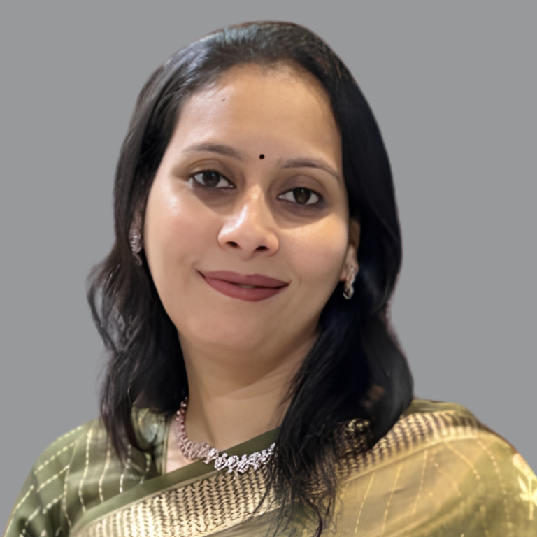 Professional portrait of Raghini Gujrati, Executive Member of Divine Sanskarshala, wearing a traditional saree with elegant jewelry and a gentle smile against a plain grey background.