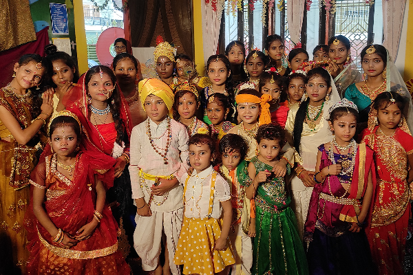 A large group of children dressed in colorful traditional Indian attire and mythological costumes pose together indoors during a Divine Sanskarshala cultural celebration. Many are wearing jewelry, crowns, veils, and festive accessories, creating a vibrant and devotional atmosphere.