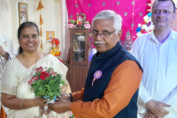 Vidya Sagar Rai, District President of BJP Varanasi, presenting a bouquet to a woman at Divine Sanskarshala during a ceremonial gathering, with other attendees standing in the background.