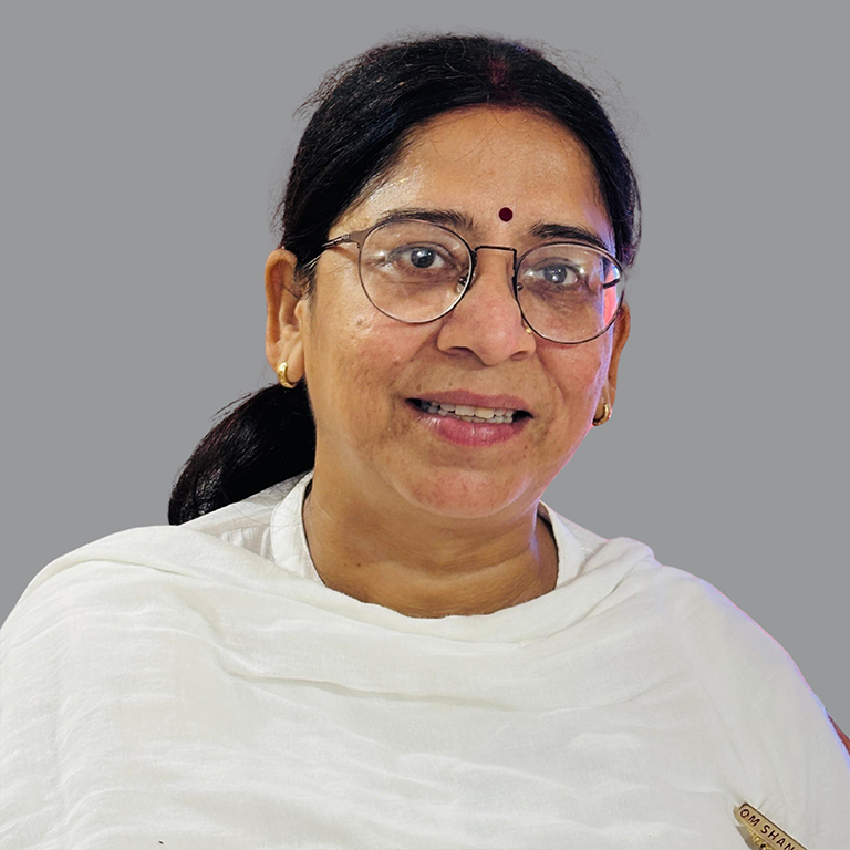 Portrait of Alpana Rai, Executive Member of Divine Sanskarshala, wearing glasses and a white traditional outfit with a small maroon bindi, smiling against a plain grey background.
