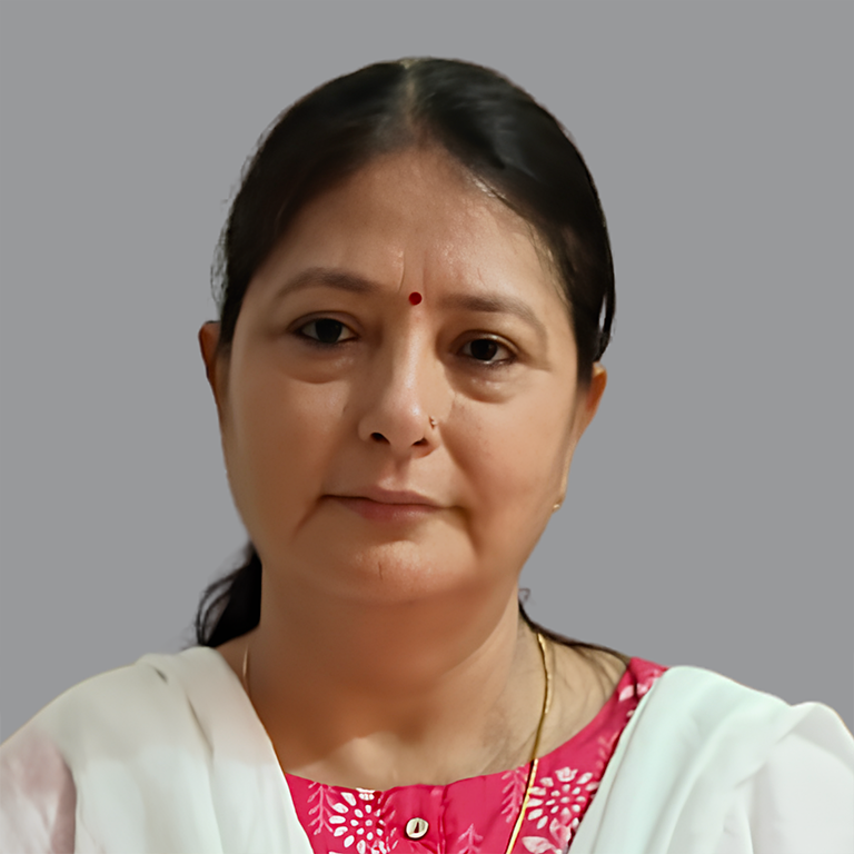 Portrait of Juhi Chopra, Executive Member of Divine Sanskarshala, wearing a pink traditional outfit with a white dupatta and a small red bindi, against a plain grey background.
