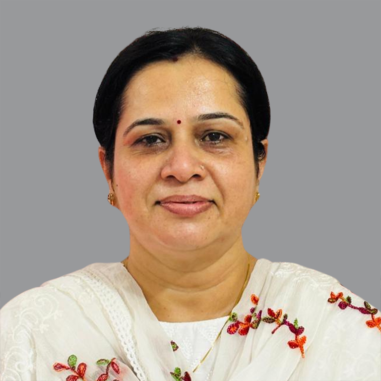 Portrait of Nidhi Kapoor, Executive Member of Divine Sanskarshala, wearing a white embroidered outfit with floral detailing and a calm expression against a grey background.