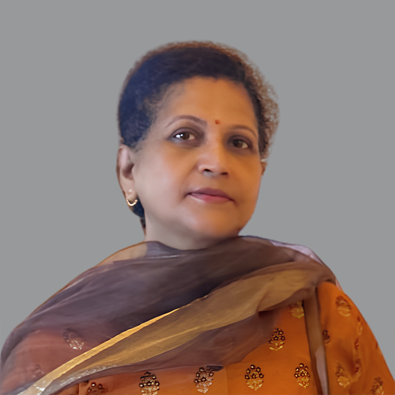 Portrait of Reeta Singh, Executive Member of Divine Sanskarshala, wearing an orange traditional outfit with a sheer brown dupatta and looking confidently toward the camera against a grey background.