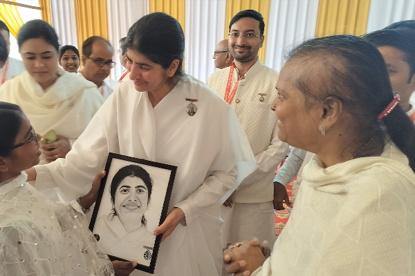 BK Shivani smiling while receiving a framed portrait gift from a student of Divine Sanskarshala, surrounded by attendees at a spiritual event.