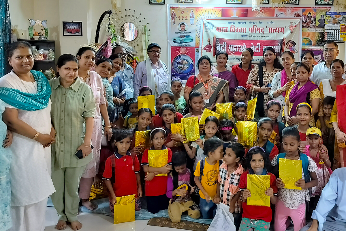 Children proudly holding gift packets alongside volunteers and club members during a community outreach and educational support program at Divine Sanskarshala.