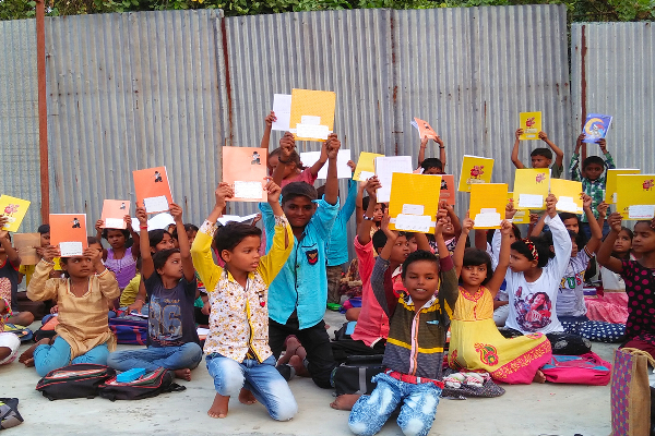 Children from a slum community proudly holding up notebooks received during an educational outreach program organized by Divine Sanskarshala, promoting learning and access to education.
