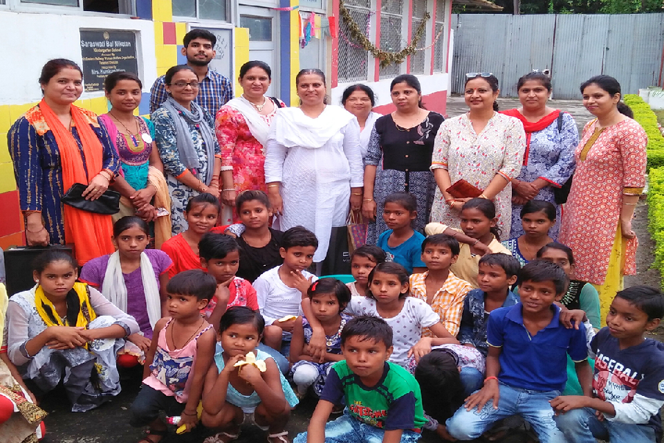 Group of volunteers and children from a slum community posing together outside Divine Sanskarshala during a community outreach and educational support program.