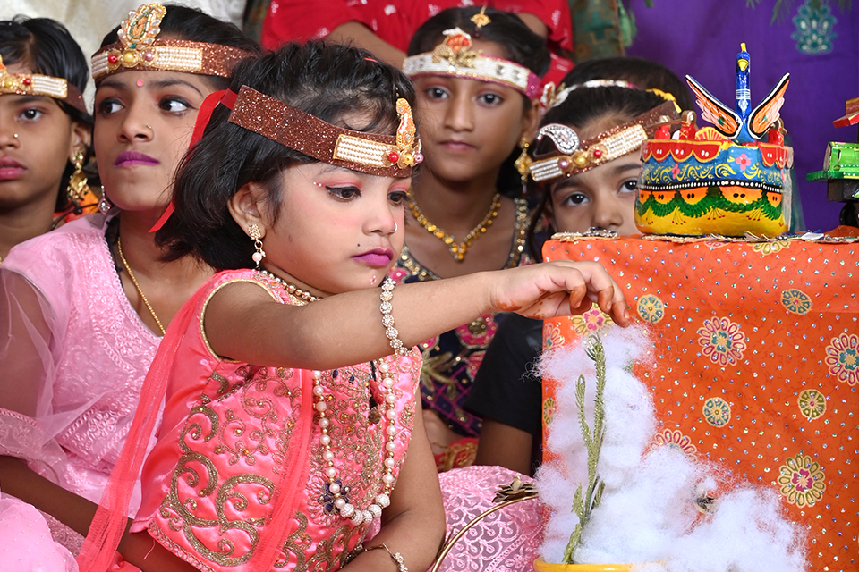 Young children from Divine Sanskarshala dressed in traditional Krishna and Radha-inspired attire participate in a Janmashtami celebration, decorating a festive display with enthusiasm and devotion.